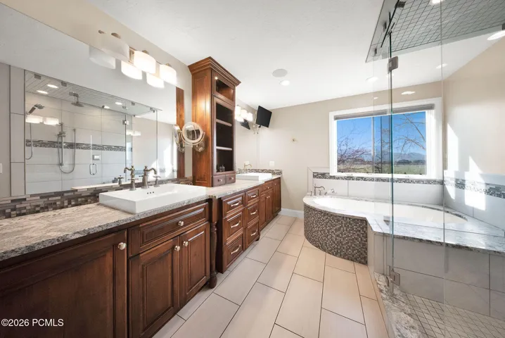 Primary bathroom featuring dual wood-finish vanity with vessel sinks, granite countertops, and full-width mirror
