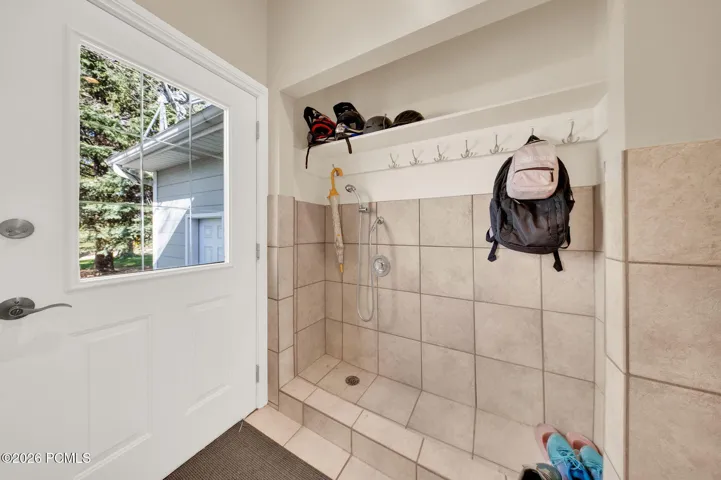 Utility area featuring a tiled wash-down zone with shower fixture, built-in shelf, and coat hooks