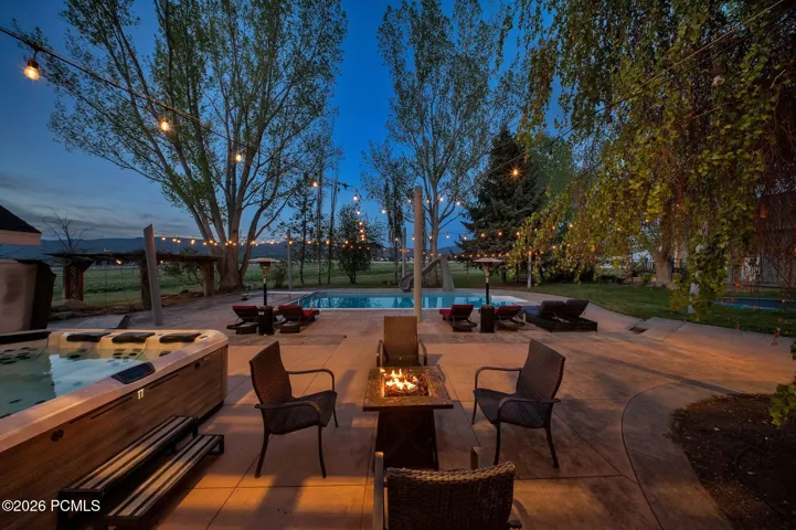 Expansive concrete patio featuring a built-in hot tub, in-ground swimming pool, and a fire pit
