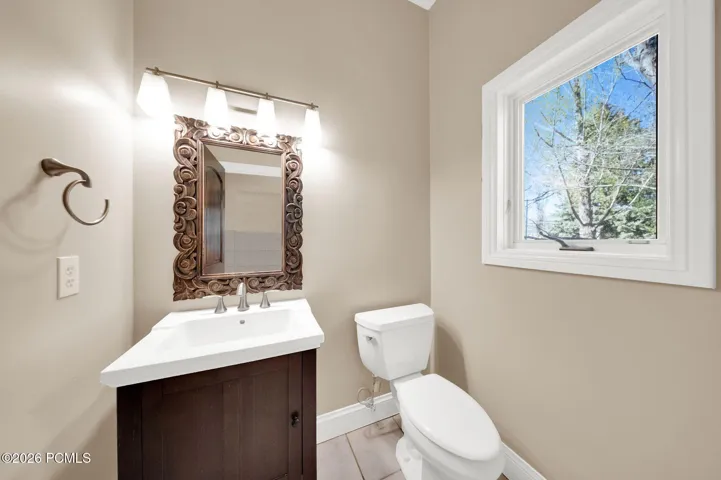 Bathroom featuring a dark wood vanity with white countertop, decorative carved wood-frame mirror, and a window with white trim