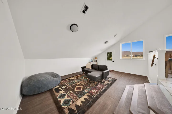 Finished loft space featuring wood-finish flooring, white vaulted ceilings, recessed lighting, and multiple windows