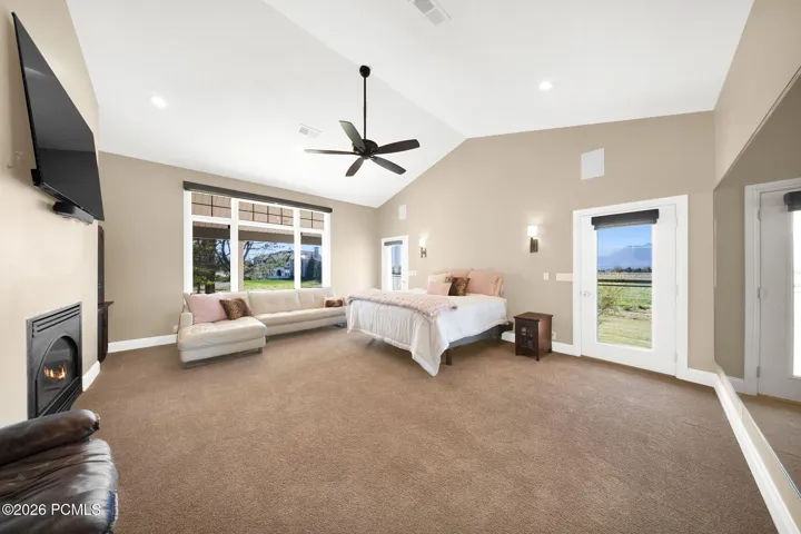Spacious Primary bedroom featuring vaulted ceilings, a ceiling fan, sconce lighting, and a fireplace with a mounted television