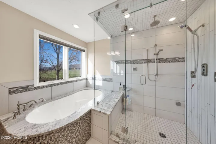 Primary Bathroom featuring a built-in soaking tub with a stone-finish deck and mosaic tile surround