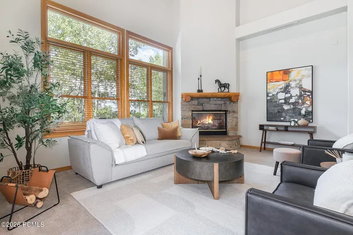 Dramatic high-volume ceiling accented by warm wood beams and glowing fireplace, creating beautiful architectural character.