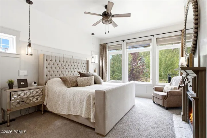 Spacious Owner's suite featuring multiple large windows, a fireplace with a detailed mantel, and a ceiling fan