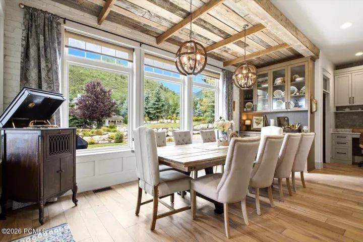 Dining area featuring large picture windows, wood-finish flooring, a wood-beamed ceiling, built-in cabinetry with glass fronts, and two spherical chandeliers