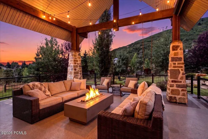 Expansive covered patio featuring a gas fire pit, exposed beam ceiling with string lights, and a view of lime canyon