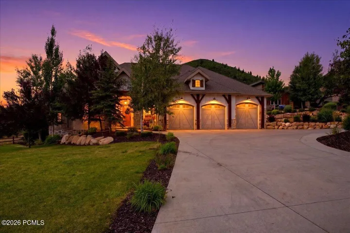Craftsman-style home featuring a three-car garage with arched wooden doors, a concrete driveway, and mature landscaping