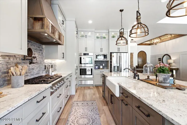 Gourmet kitchen featuring a farmhouse sink, stainless steel appliances, light-colored cabinetry, and a natural wood range hood