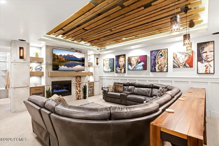 Spacious recreation room featuring a linear gas fireplace, built-in shelving, wood-finish ceiling accents, and wainscoting