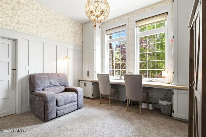 Office featuring two large grid-pane windows with integrated desk space, built-in lower cabinetry, decorative wallpaper, and board and batten wall detailing