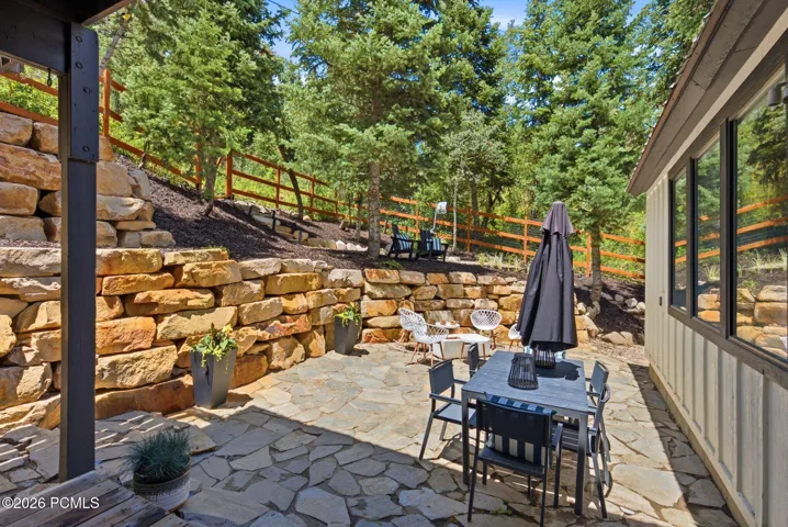 Private backyard with expansive flagstone patio area with natural stone retaining walls and mature evergreen trees