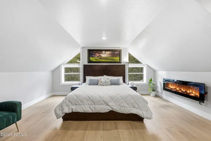 Gorgeous primary suite with vaulted ceilings, radiant floor heating, and a contemporary wall-mounted electric fireplace