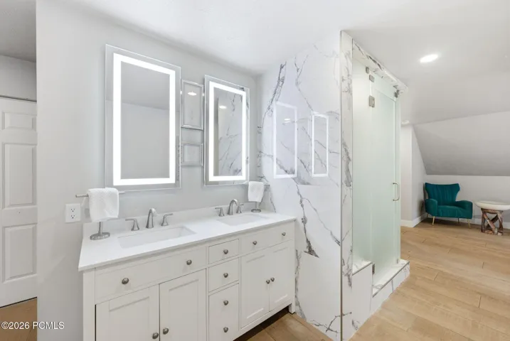 Dual vanity with white cabinetry, integrated sinks, and illuminated mirrors. Large primary shower