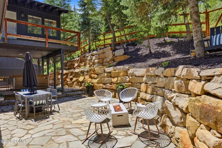 Private backyard extensive flagstone patio with a fire pit, stone retaining walls, and mature tree landscaping