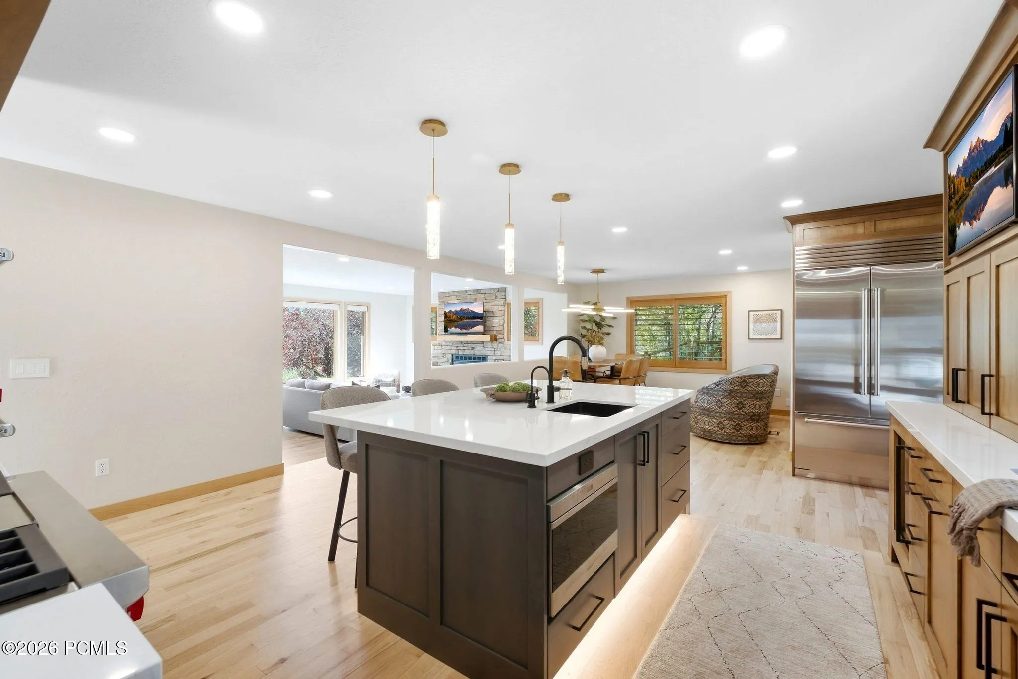 Kitchen island with quartz countertops, stainless steel Sub-Zero refrigerator, updated lighting, and refinished wood-finish flooring.
