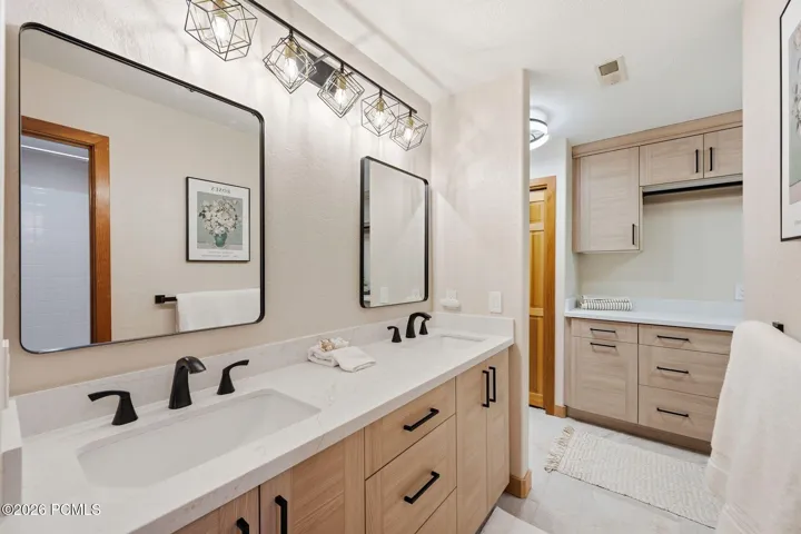 Dual vanity with integrated sinks and matte black fixtures with Valor Gold Lava quartzite countertops, heated floors, and updated lighting.