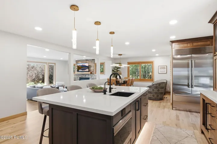 Kitchen island with quartz countertops, stainless steel Sub-Zero refrigerator, updated lighting, and refinished wood-finish flooring.