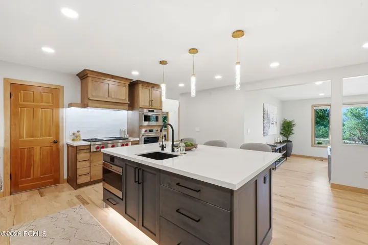 Updated kitchen featuring a large island with quartz countertops and high-end two-tone cabinetry, stainless steel appliances (Wolf and Sub-Zero), refinished wood flooring, and updated lighting