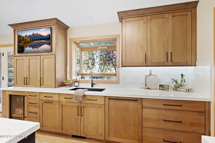 High end wood-finish cabinetry with matte black hardware, Ethereal Glow Quartz countertops, built-in beverage center, recessed lighting, and a glass-paned door opening to the back deck and outdoor seating areas