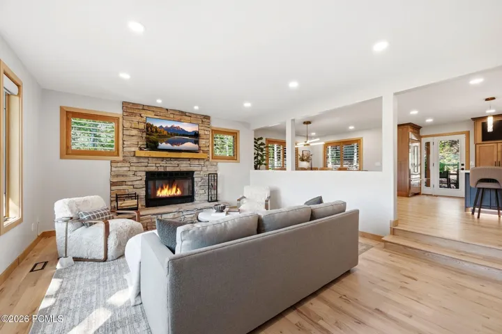 Stone-faced fireplace with a natural wood mantle, updated recessed lighting, refinished wood flooring, open concept to the kitchen and dining areas, and wood-casing windows with wooden shutters.