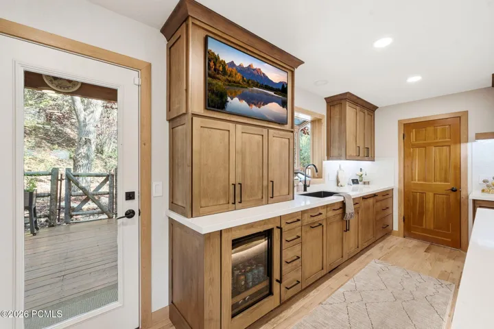 High end wood-finish cabinetry with matte black hardware, Ethereal Glow Quartz countertops, built-in beverage center, recessed lighting, and a glass-paned door opening to the back deck and outdoor seating areas