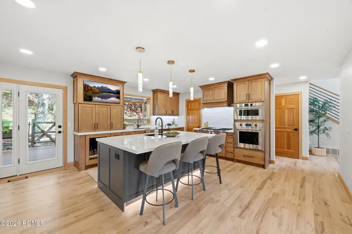 Kitchen featuring a center island with under-cabinet lighting, stainless steel double Wolf ovens (convection and steam), high-end wood-finish cabinetry, and light refinished wood flooring