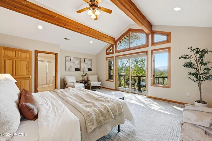 Primary bedroom featuring exposed wooden beams, private balcony, fireplace, seating area, ensuite bathroom with heated floors, a jetted tub, stand alone shower, and walk-in closet. Wake up to the incredible views of the mountains.