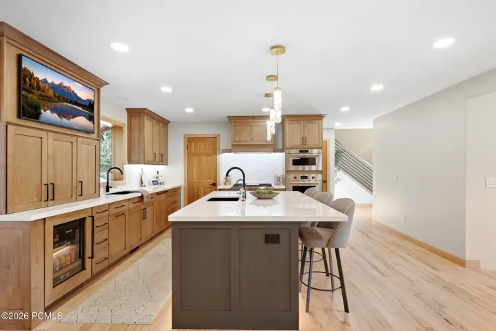 Updated kitchen featuring a large island with quartz countertops and high-end two-tone cabinetry, stainless steel appliances (Wolf and Sub-Zero), refinished wood flooring, and updated lighting