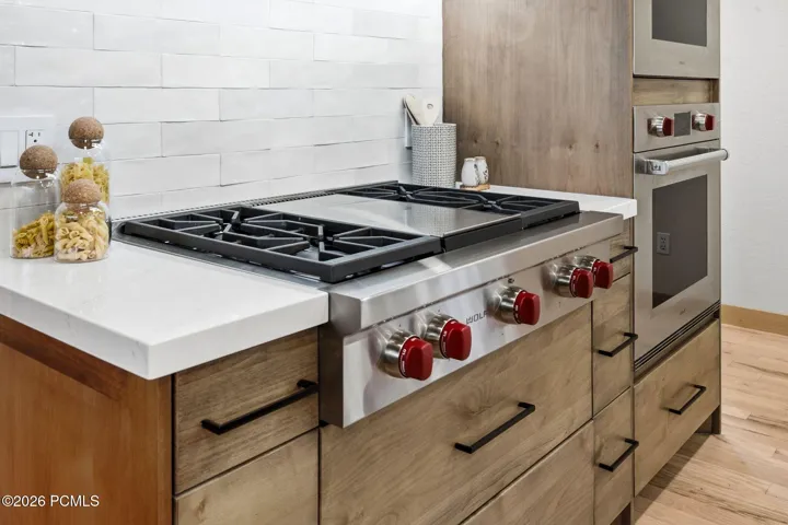 Stainless steel Wolf gas range with, 2 built-in stainless steel Wolf ovens (Convection/conventional and steam), quartz countertop, and high-end natural wood cabinetry.