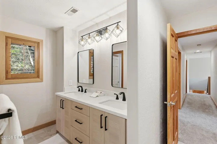 Dual vanity with integrated sinks and matte black fixtures with Valor Gold Lava quartzite countertops, heated floors, and updated lighting.