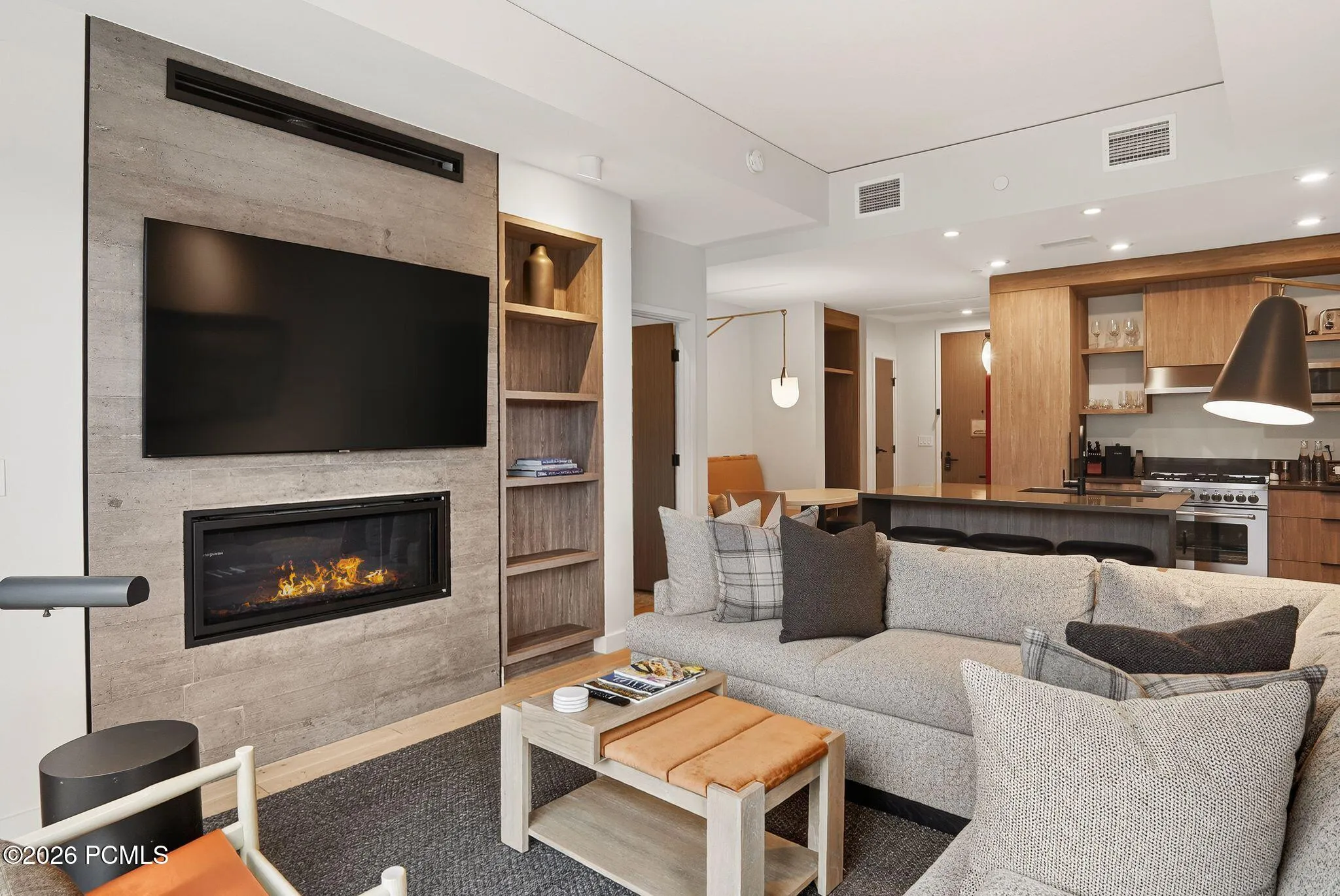Linear gas fireplace and mounted television anchor the great room with the kitchen open beyond.