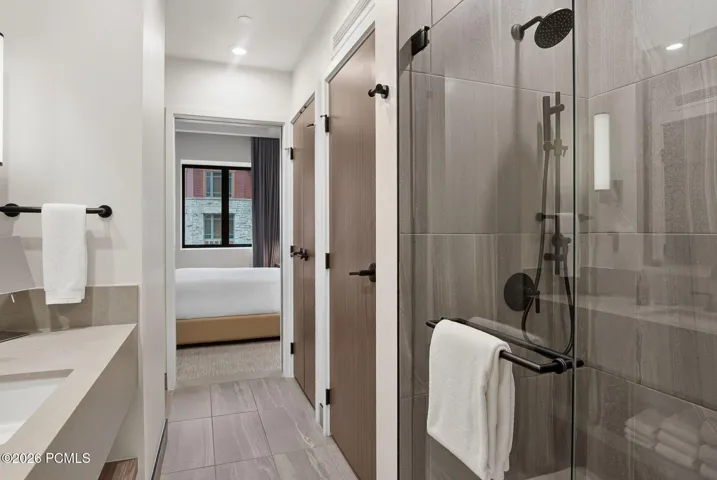Primary bath vanity and glass enclosed shower with the bedroom beyond.