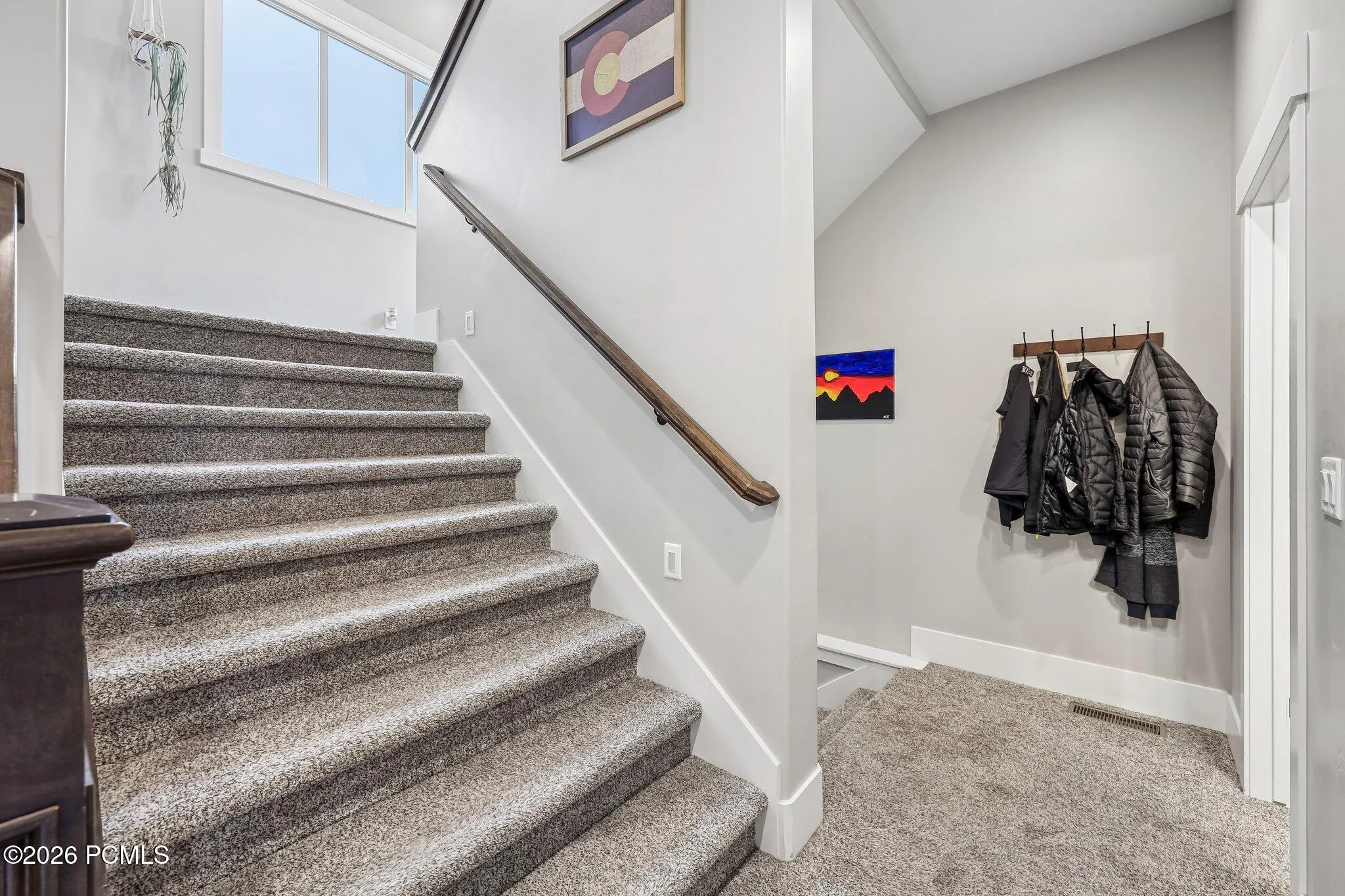 Carpeted staircase connecting three levels, with coat hooks at the landing, inside a Rustler at Hideout home in Hideout, Utah.