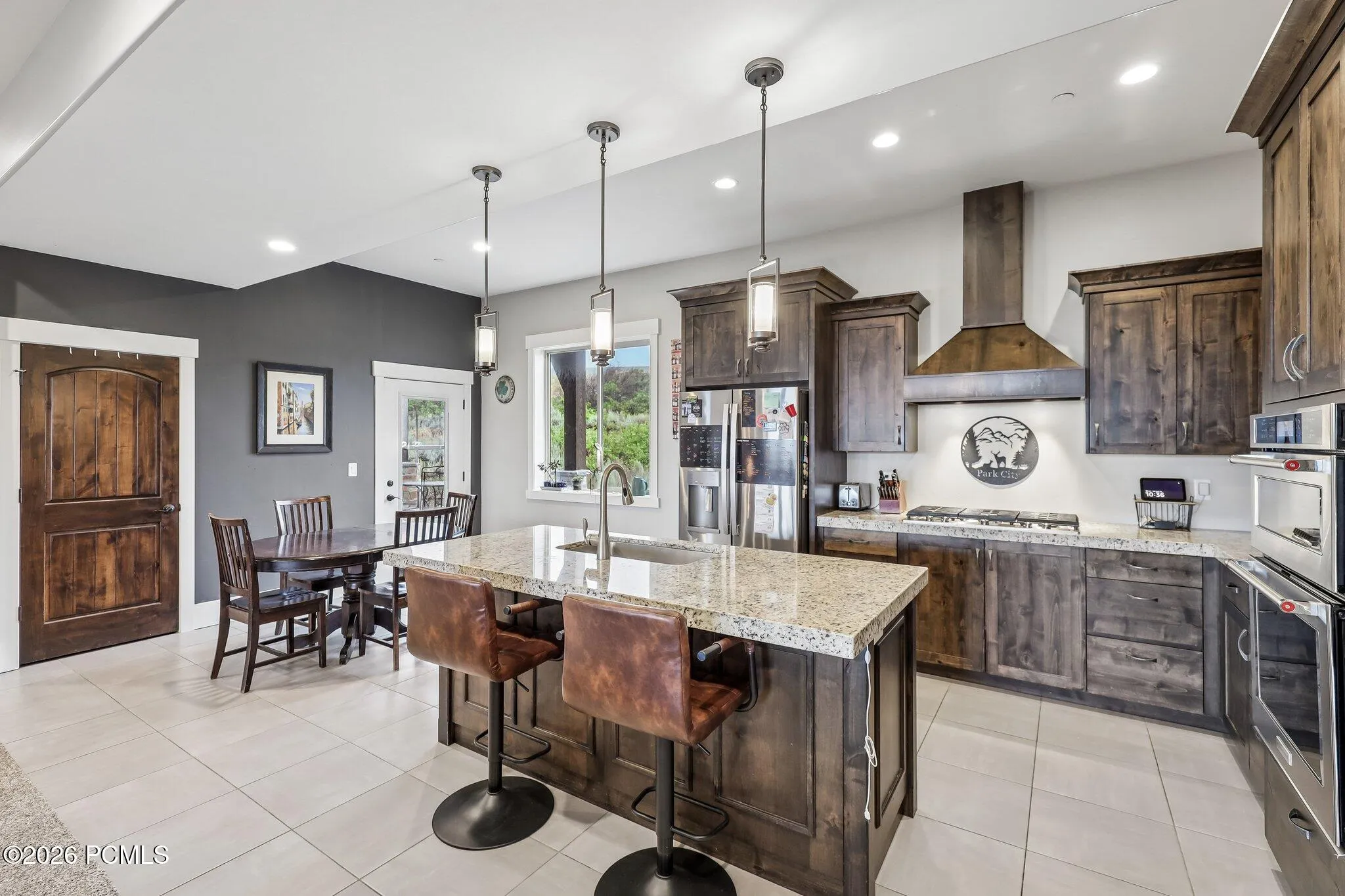 Kitchen with a granite island with bar seating, stained wood cabinetry and a vent hood in a Rustler at Hideout home in Hideout, Utah.