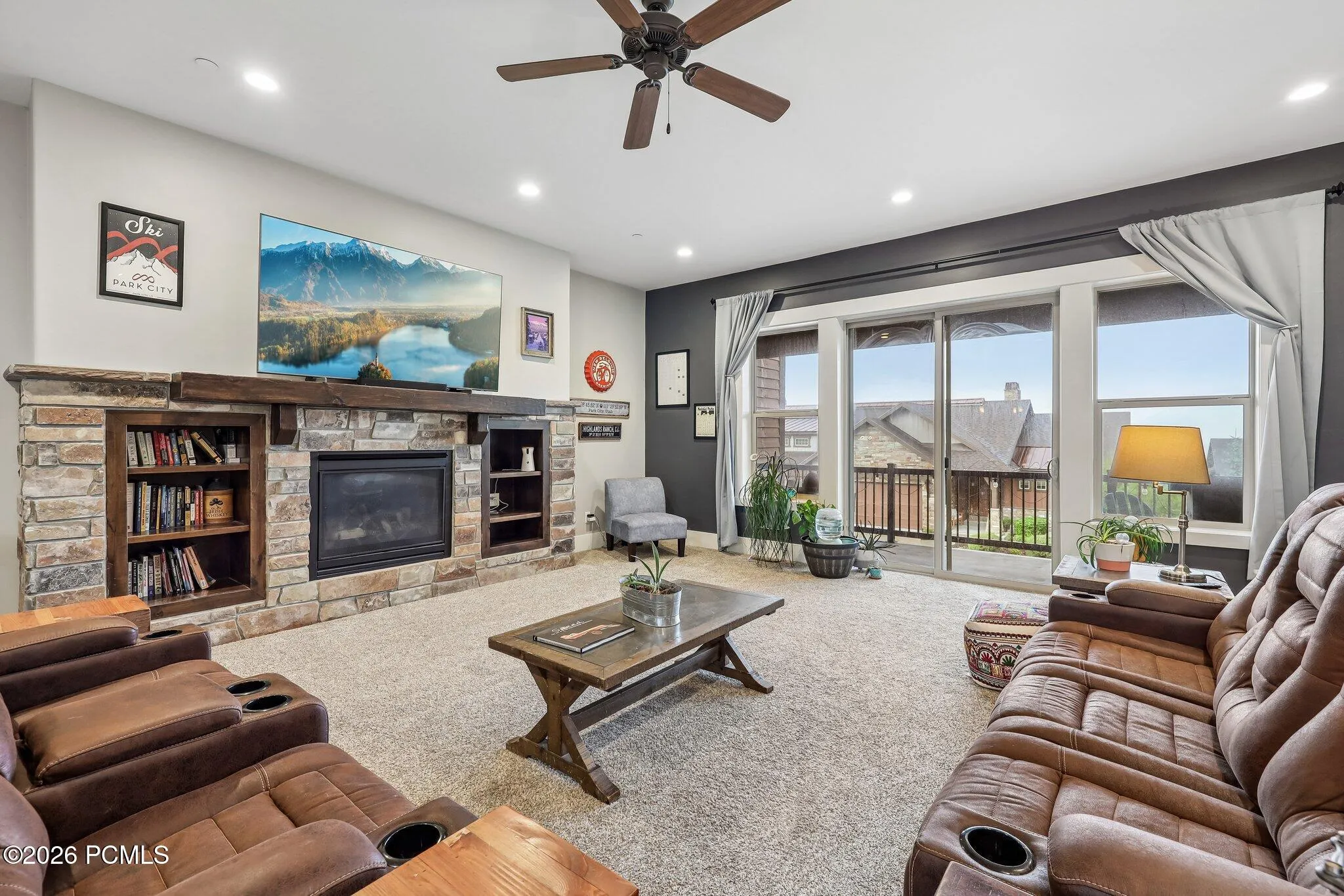 Great room with a stone fireplace and a glass slider to the covered deck, framing Wasatch Back and Jordanelle Reservoir views from Hideout, Utah.