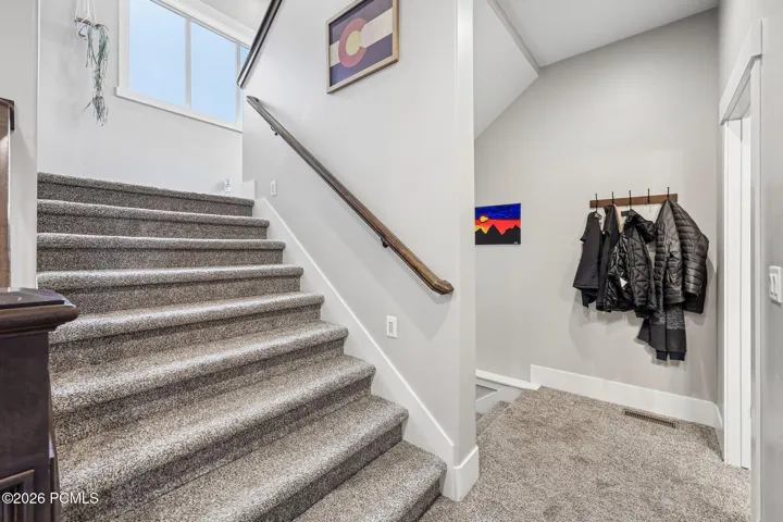 Carpeted staircase connecting three levels, with coat hooks at the landing, inside a Rustler at Hideout home in Hideout, Utah.