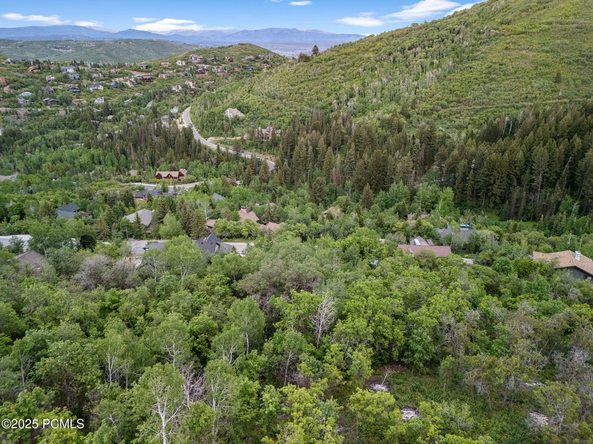Long views across the Pinebrook canyon toward the surrounding Wasatch peaks, with aspen and pine hillsides and established Park City mountain homes above.