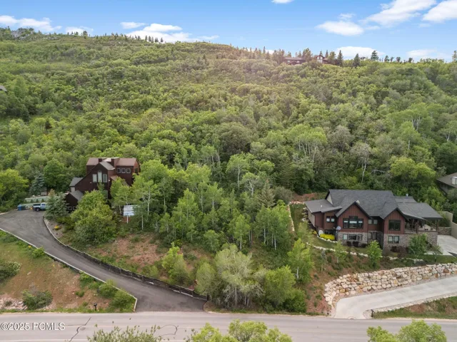 Elevated 0.65-acre Pinebrook homesite on Stagecoach Drive in Park City, framed by mature aspens and pines with mountain views and established custom homes on either side.