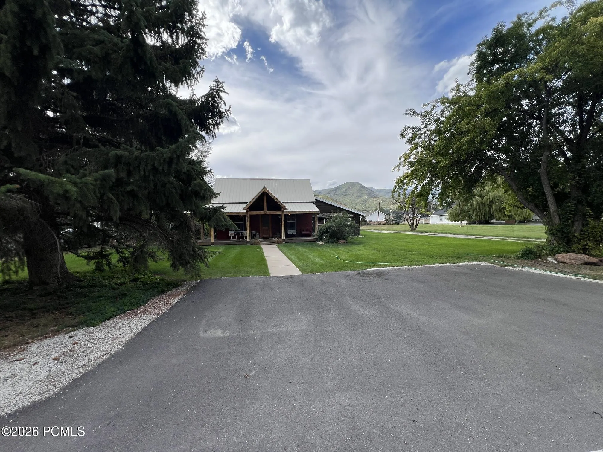 Asphalt Parking pad leading to a residence front door, covered front porch with wood columns, and a landscaped front lawn