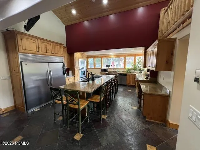 Kitchen featuring a large center island with seating, stainless steel appliances, wood cabinetry, and a vaulted wood-paneled ceiling