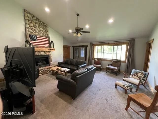 Stone-clad fireplace with wood mantel, vaulted ceiling with recessed lighting, ceiling fan, and extensive window with wood trim