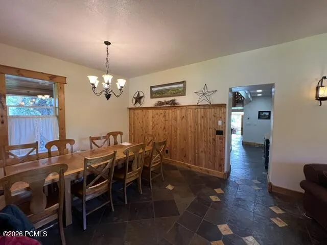 Stone tile flooring with accent tiles, wood panel wainscoting, wood-trimmed window, and a five-light chandelier