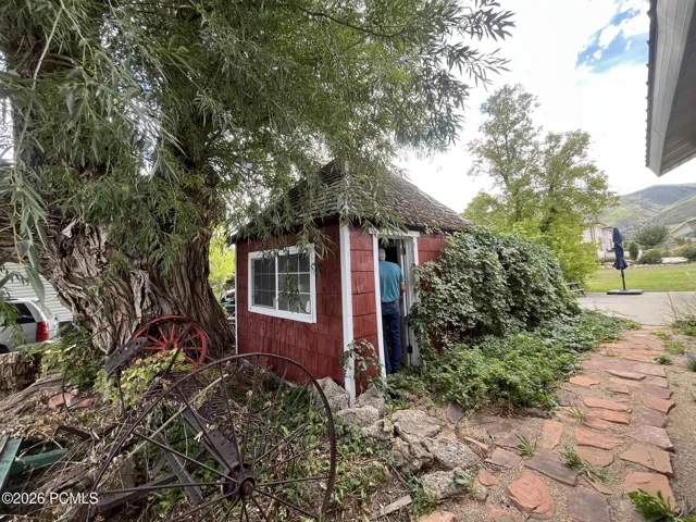 Red-sided storage shed with white-framed window, surrounded by mature trees and lush greenery