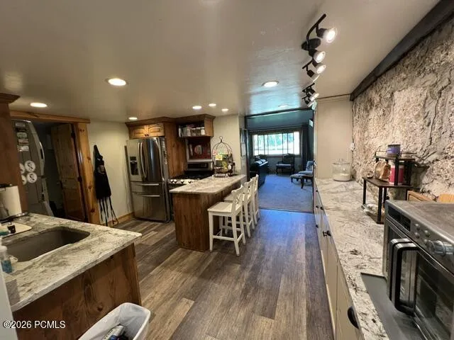 Wood-finish flooring, stone accent wall, recessed lighting, track lighting, and stainless steel appliances