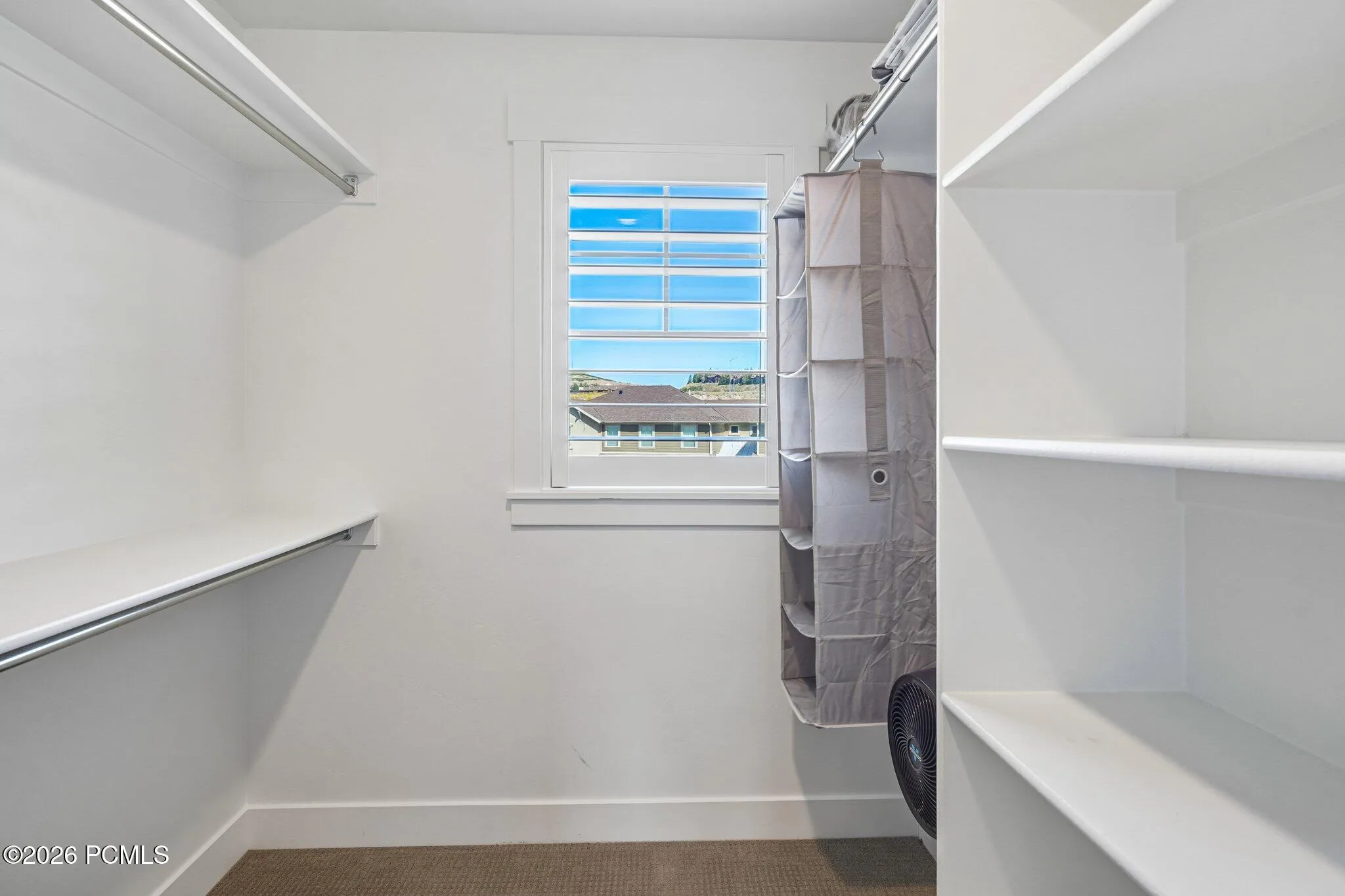 Primary walk-in closet with built-in shelving and a window.
