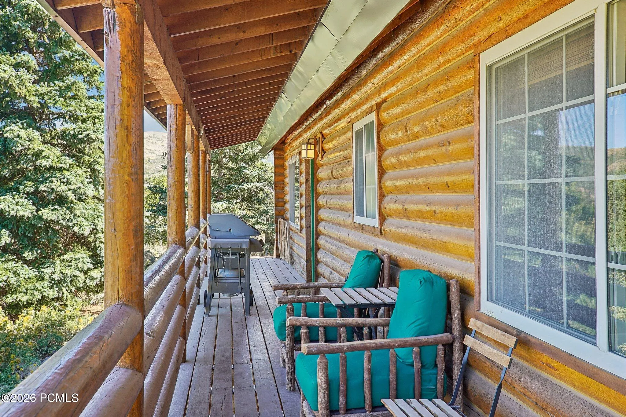 The covered deck runs the full width of the house, with the grill at one end, seating at the other, and shade when the afternoon calls for it.The covered deck runs the full width of the house, with the grill at one end, seating at the other, and shade when the afternoon calls for it.Covered deck running the width of the log home with log railings, outdoor seating, and a grill.