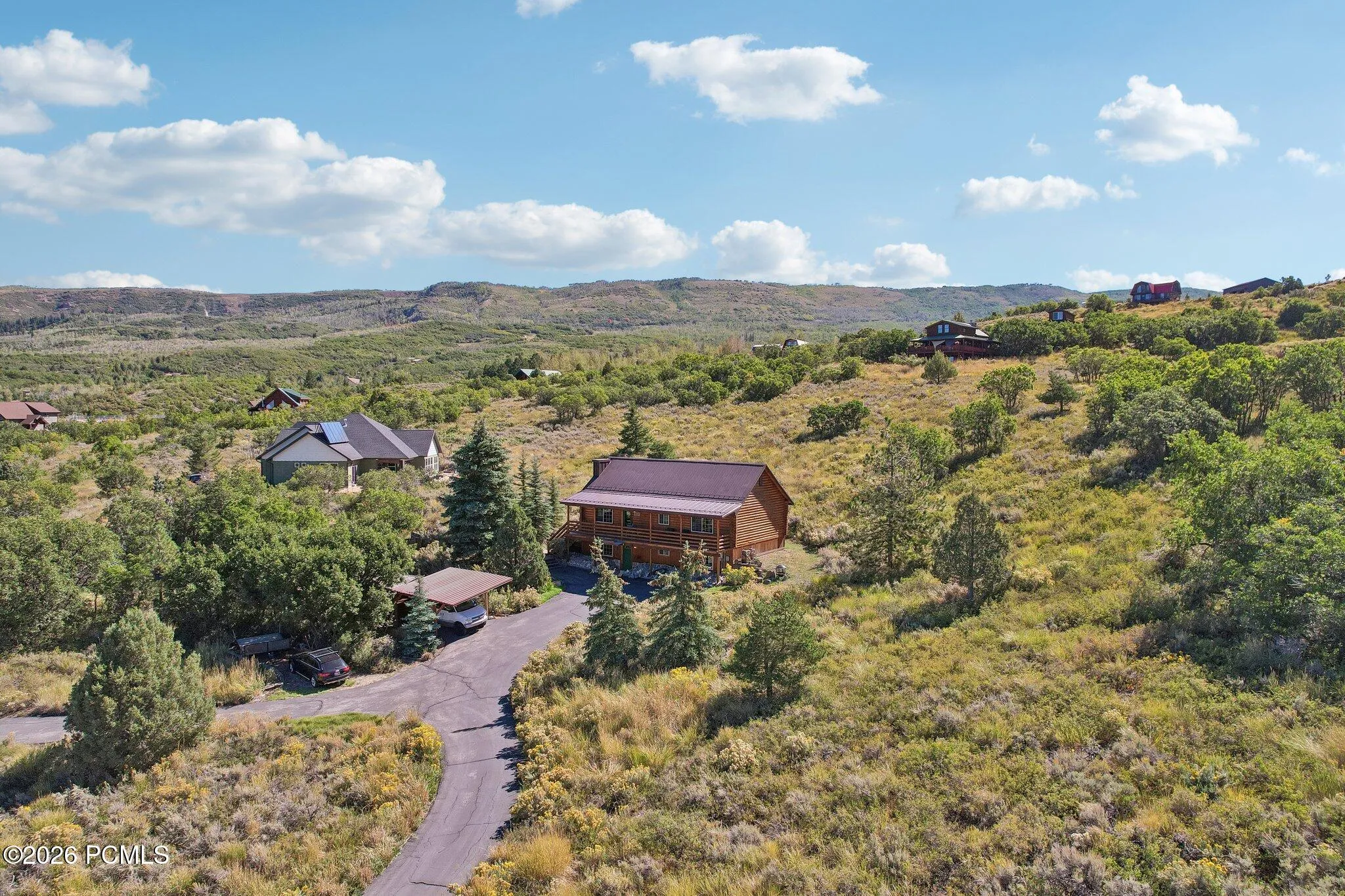 An aerial over Timber Lakes showing how homesites settle into the sagebrush with ridgelines behind them. The space between houses is the appeal.An aerial over Timber Lakes showing how homesites settle into the sagebrush with ridgelines behind them. The space between houses is the appeal.Aerial view of the log home and surrounding Timber Lakes homesites, with sagebrush hillsides and mountain ridgelines beyond.