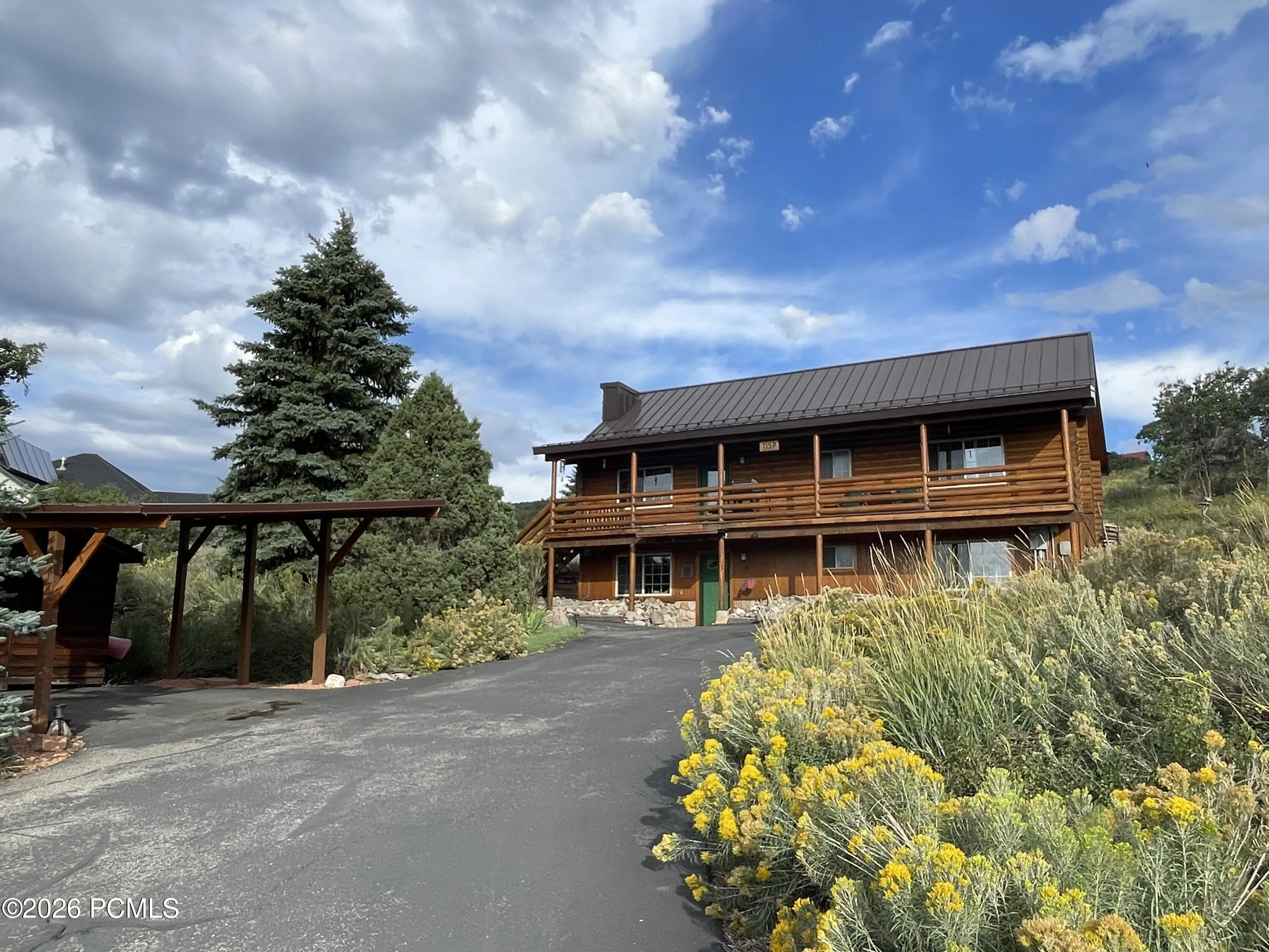 The circular driveway means no backing down the hill, and the covered carport keeps a vehicle out of the snow. Mature pines and native rabbitbrush line the drive.