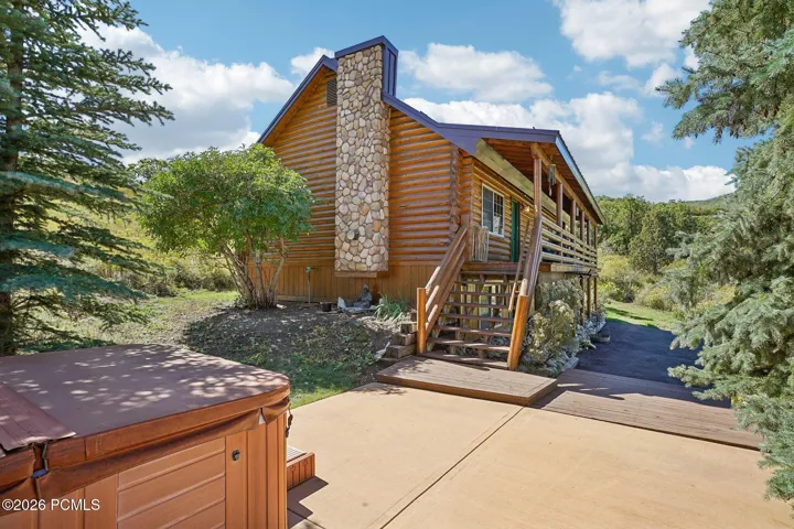 Stone chimney, stairs up to the deck, patio below, and the hot tub in easy reach. The full outdoor setup in a single frame.